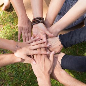 Top view of stack of hands against green grass. Friendship, teamwork or community gesture. Unity or team concept